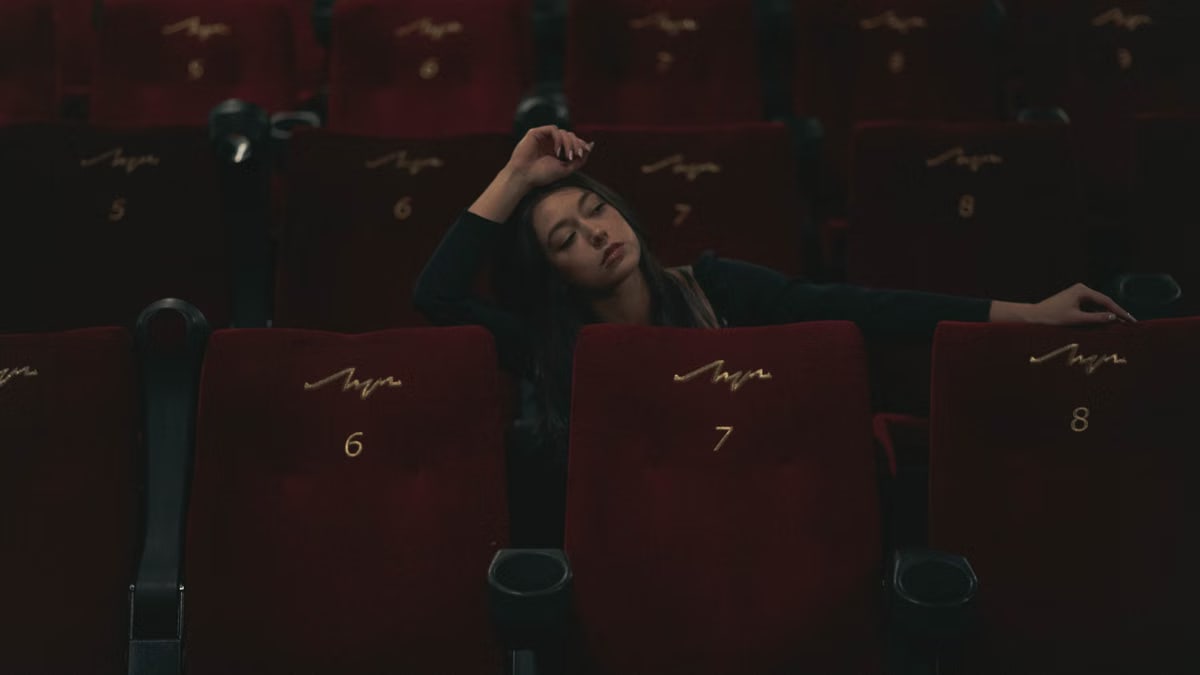 A woman in black long sleeves sitting in an empty theater, surrounded by red seats.